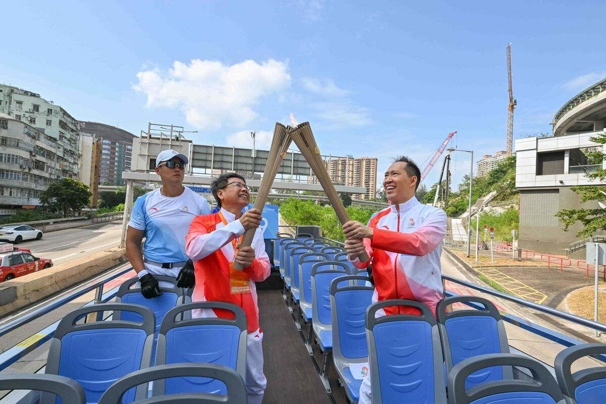 接力傳遞:  火炬手乘坐開篷巴士至啟德體育園巴士站。第38棒火炬手黃永光（右）把火種傳給第39棒火炬手鍾澤文。