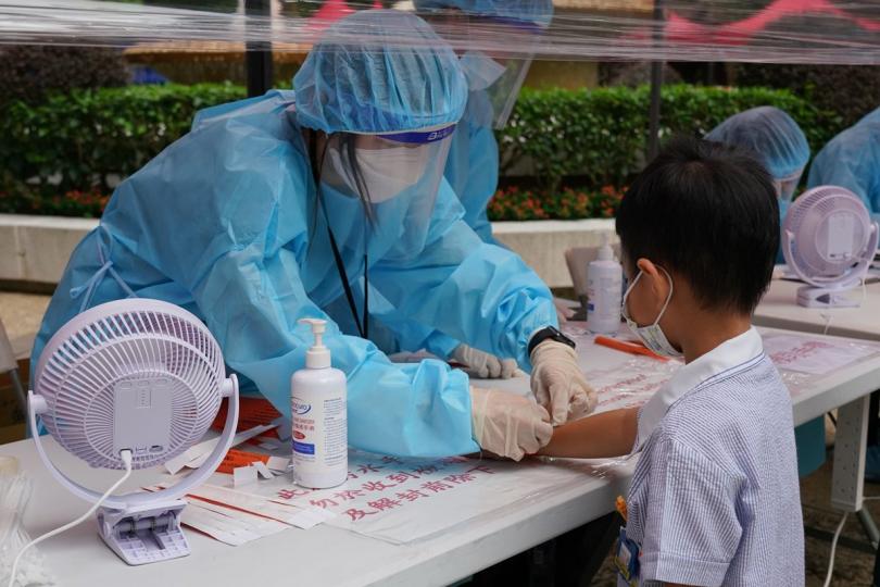 以資識別:  參與圍封行動的漁農自然護理署人員在華盛閣受限區域，為已接受強制檢測的居民佩戴手環。