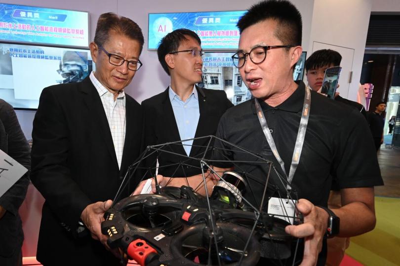 嶄新技術:  陳茂波（左）聽取有關人工智能無人機外牆剝落/滲水檢測系統的介紹。