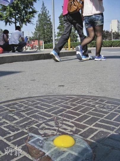 本報記者打了一隻雞蛋在北京一處渠蓋上，看着它慢慢變成半生熟。（劉洪慶攝）