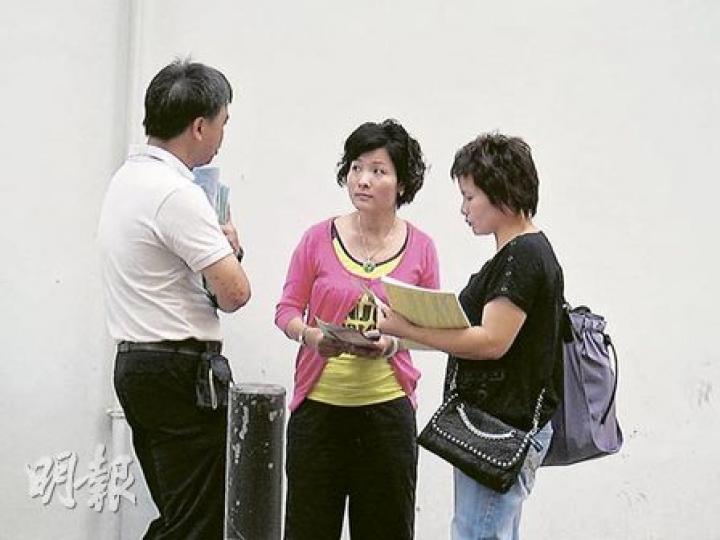 深培中學昨安排教師（左）在呂祺教育服務中心門外，向剛在中心領取註冊證的家長（中和右）派發傳單，講解學校各項支援新生的措施及資助。（陳嘉婉攝）