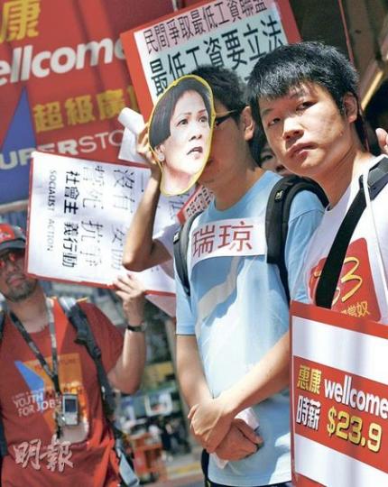 有團體調查發現零售業員工的整體時薪為25.08元，其中一間元朗區7-Eleven分店時薪更低至20元。團體昨到銅鑼灣一家超市門外抗議，戴上臨時最低工資委員會成員麥瑞琼的面具上演街頭劇，諷刺她同時兼任低薪企業的高層，有帶頭壓低員工福利之嫌。（林振東攝）