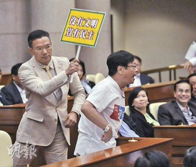 當社民連黃毓民（右）破口大罵、抗議曾蔭權不回應提問時，旅遊界謝偉俊忽然走到他背後，舉牌「作狀」要拍打黃毓民。（葉漢華攝）