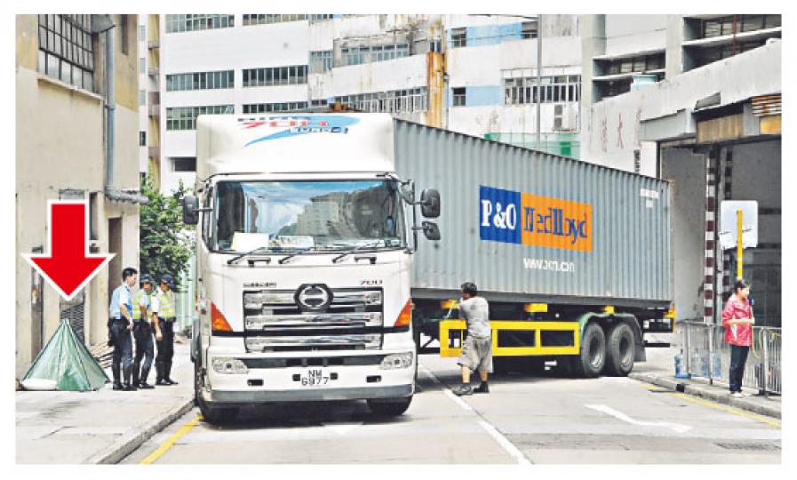 貨櫃車剛從工業大廈轉出街便遇上交通燈亮起紅燈，車身橫跨兩線停下，當車再起步時撞死「攝車罅」老婦，屍體被抬到行人路以帳篷蓋住（箭嘴示）。（劉友光攝）貨櫃車司機涉危險駕駛導致他人死亡被捕。（劉友光攝）