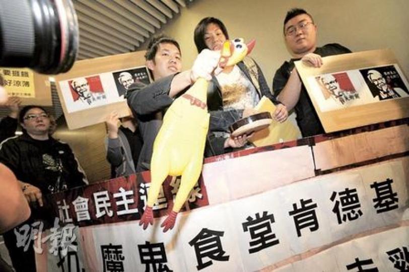 大家樂撤銷扣減「飯鐘錢」安排後，民間力量轉盯另一間沒向員工發用膳時薪的快餐店肯德基（KFC）。社民連成員昨帶同「塑膠玩具雞」到荃灣如心廣場肯德基寫字樓抗議，諷刺肯德基員工被「榨乾榨盡」。 （何家達攝）