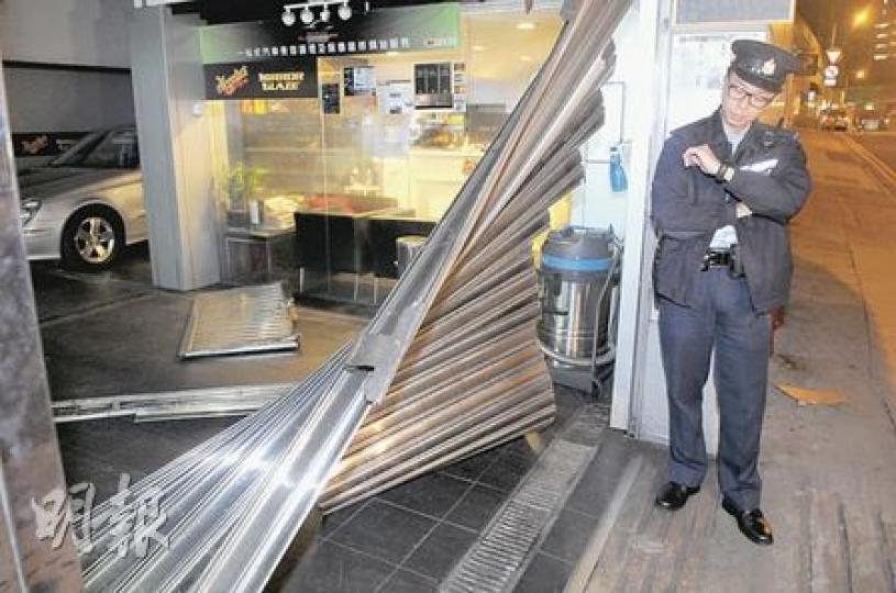 車房捲閘被撞後嚴重變形鬆脫,警員事後看守現場等候東主返回助查。(蔡方山攝) 車房捲閘被撞後嚴重變形鬆脫,警員事後看守現場等候東主返回助查。(蔡方山攝)