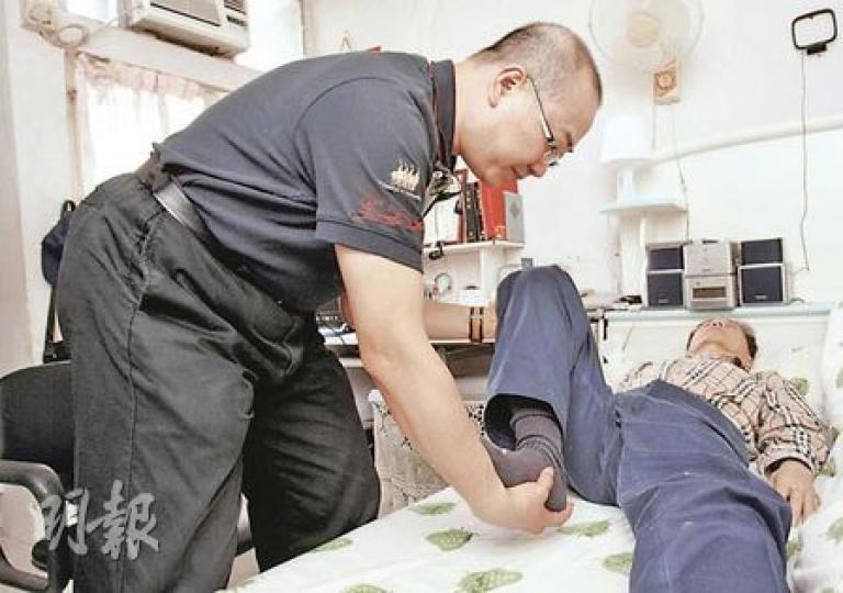 趙崇偉（左一）學習按摩課程後，由生意人變身按摩員，為70歲的郭伯伯（躺臥者）治療坐骨神經痛，經十多次按摩治療後，伯伯原本無法彎曲的膝蓋已恢復活動能力。（陳智良攝）