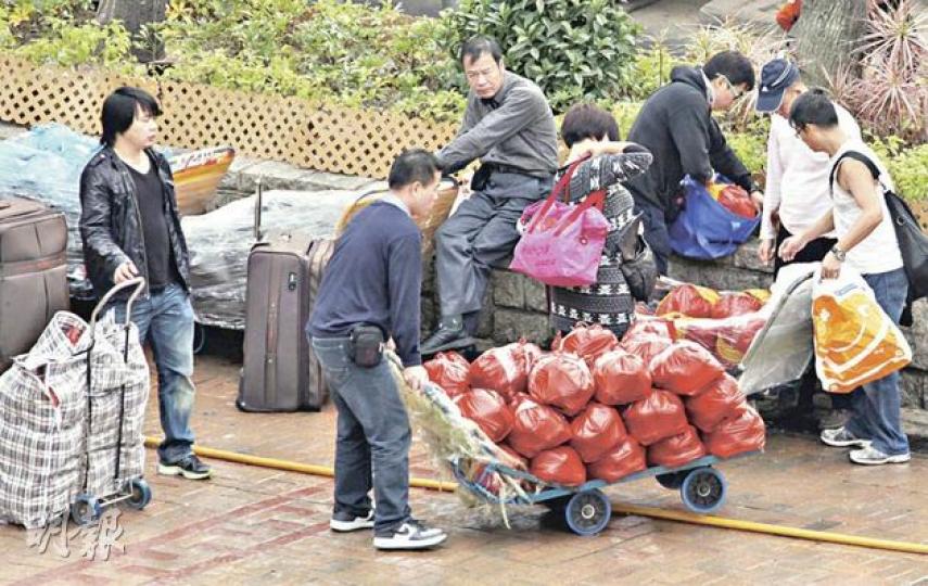 在上水貨車站外昨結集大批水貨客，圖中男子手推車上一袋袋紅色膠袋內，其實是疑走私返內地的鮮活龍蝦。記者採訪時見袋中有龍蝦的觸鬚及存放龍蝦包裝盒內的木糠。（林錫禮攝） 港鐵附例特檢隊人員（左）昨於上水站執勤時，因懷疑檢查水貨客的違規過大行李，被水貨客推至牆邊及「叉頸」襲擊，結果要送院檢查。（林錫禮攝）