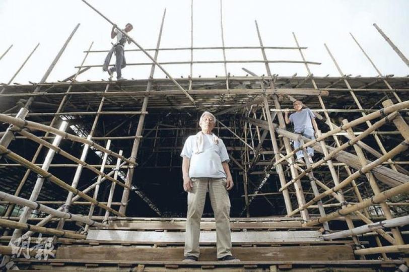 戲棚建築結構複雜,由數以千計竹枝和杉木搭成,卻不用一口釘,72歲的老師傅黎錦棠(中)不用工具量度,只憑雙眼一看,在地上指點工人,就可以準確無誤搭起戲棚。他形容戲棚就像少林寺,「識做戲棚,唔使學都識做地盤同維修」。右為黎的徒孫陳太祥,左是竹棚業新生代張慧安,3人正趕工為大埔天后誕搭戲棚。(余俊亮攝) 戲棚建築結構複雜,由數以千計竹枝和杉木搭成,卻不用一口釘,72歲的老師傅黎錦棠(中)不用工具量度,只憑雙眼一看,在地上指點工人,就可以準確無誤搭起戲棚。他形容戲棚就像少林寺,「識做戲棚,唔使學都識做地盤同維修」。右為黎的徒孫陳太祥,左是竹棚業新生代張慧安,3人正趕工為大埔天后誕搭戲棚。(余俊亮攝)