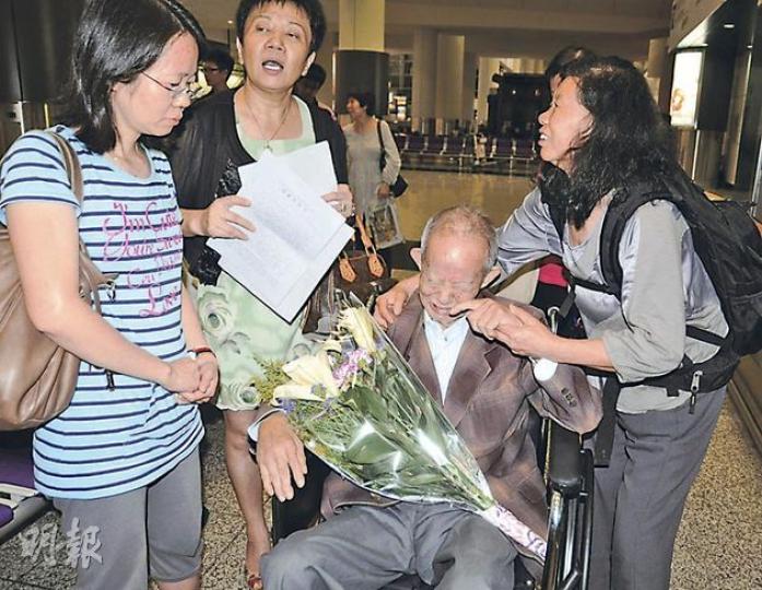 王文金（坐輪椅者）由妻子黃亞珍（右）及女兒用輪椅推出香港機場時，老淚縱橫，港商內地投資權益關注組召集人陸偉萍（左二），則獻上一束鮮花慰問。（明報記者攝）