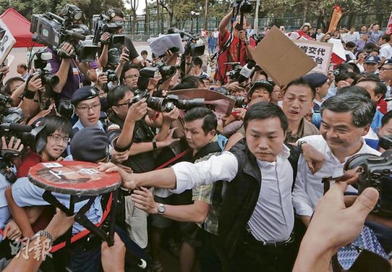 特首梁振英（前排右一）昨日到黃大仙時需警方開路才可進入會場，原本他計劃到請願區接信，但最終由警方護送下直接入會場。社民連將貼上梁振英肖像和寫有「下台」兩字的摺櫈遞到梁振英面前，隨即被G4擋開。（李澤彤攝）