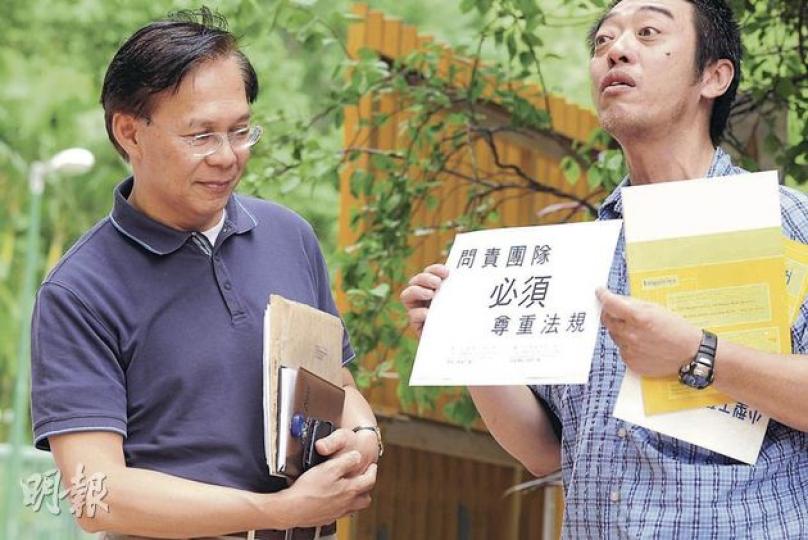 發展局長麥齊光（左）昨到東涌出席居民諮詢會前，有示威者向他遞上信件及兩本屋宇署處理違規建築的小冊子，促請各官員檢查住宅有沒有僭建物。（鄧宗弘攝）