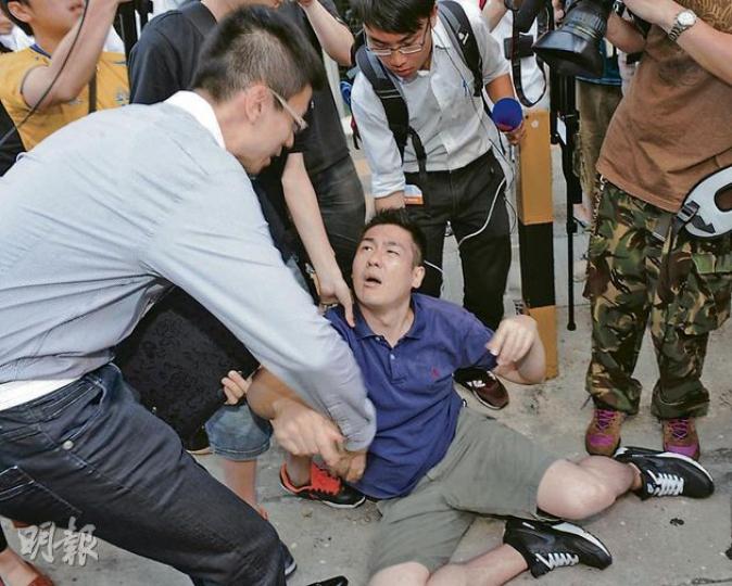 新聞秘書羅莘桉（左）昨護送政務司長林鄭月娥離開期間，被指推倒欲向林太交示威物品的譚姓男子（中），羅其後扶起該男子，二人均被帶署助查。（劉焌陶攝）有示威者指控被林鄭月娥的新聞秘書羅莘桉推倒，羅莘桉被帶上警車返署協助調查。（劉焌陶攝）