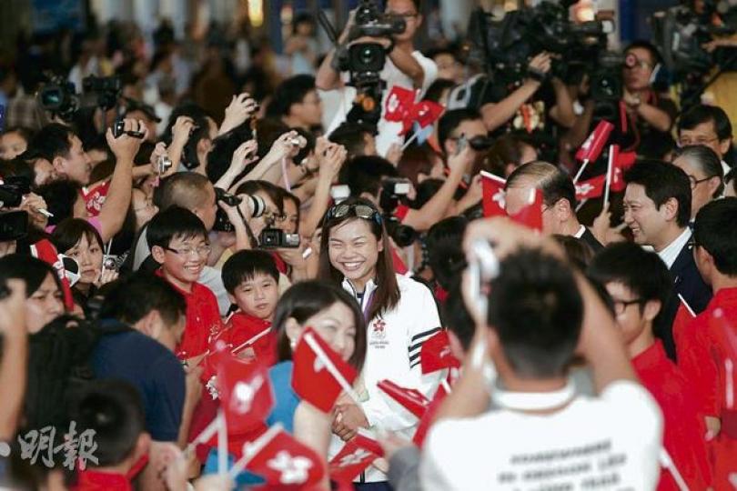 政府為一眾香港奧運代表團運動員舉行歡迎儀式，為本港單車隊於今屆奧運取得「零的突破」的李慧詩（中），甫踏入接機大堂即獲大批小朋友手持區旗夾道歡迎，李慧詩笑得合不攏嘴。（李紹昌攝） 在今屆倫敦奧運摘銅的李慧詩（右四），昨日隨香港奧運代表團返港，在政府於機場舉行的歡迎儀式中，與教練沈金康（右三）、「師兄」黃金寶（右一）及一眾單車隊隊員合照。（李紹昌攝）