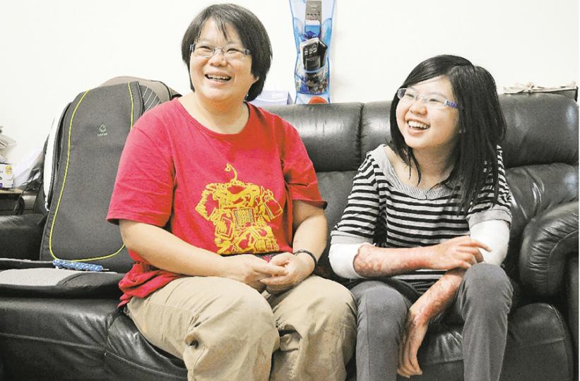 白加士街違規唐樓火警倖存者鄧岢娭(右),全身嚴重燒傷,雙腳肌肉大量壞死,瘦得剩下骨頭,長短腳更令她舉步維艱。但岢娭與母親(左)生性樂觀,每天在歡笑聲中重過新生。她們呼籲全港市民,不要再忍受身邊的樓宇違規,必須迫使政府執法改善,「不要怕事,一定要出聲,那關乎你條命!」(明報記者攝) 白加士街違規唐樓火警倖存者鄧岢娭(右),全身嚴重燒傷,雙腳肌肉大量壞死,瘦得剩下骨頭,長短腳更令她舉步維艱。但岢娭與母親(左)生性樂觀,每天在歡笑聲中重過新生。她們呼籲全港市民,不要再忍受身邊的樓宇違規,必須迫使政府執法改善,「不要怕事,一定要出聲,那關乎你條命!」(明報記者攝)