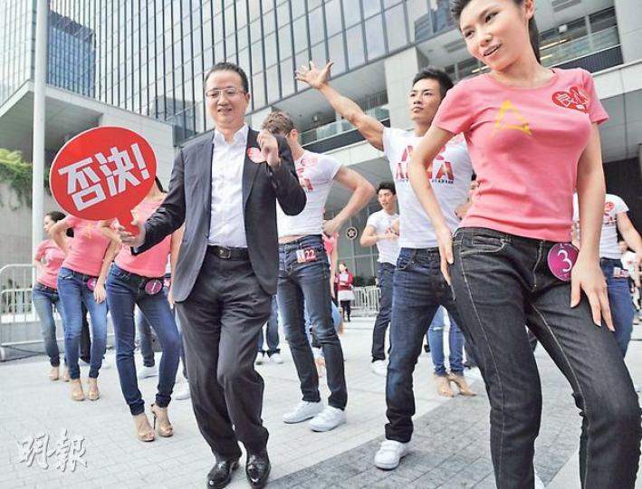 亞洲電視投資者王征（前左）昨日全程手舉「否決」紙牌。於眾亞姐及藝員綵排期間，他更突然站於眾藝員前「領舞」，大跳「江南Style」。（葉家豪攝）立法會議員毛孟靜（左下角）走進集會現場，欲與王征（右上角）對話，二人隔着亞洲先生候選人的人牆起爭執，其間王征更叫毛「滾回去」。（盧翊銘攝）一眾員工出席亞視的反對濫發牌照集會，有員工更帶同子女出席，並表示讓他們來「見識吓」，眾人須負責高舉示威牌。（盧翊銘攝）