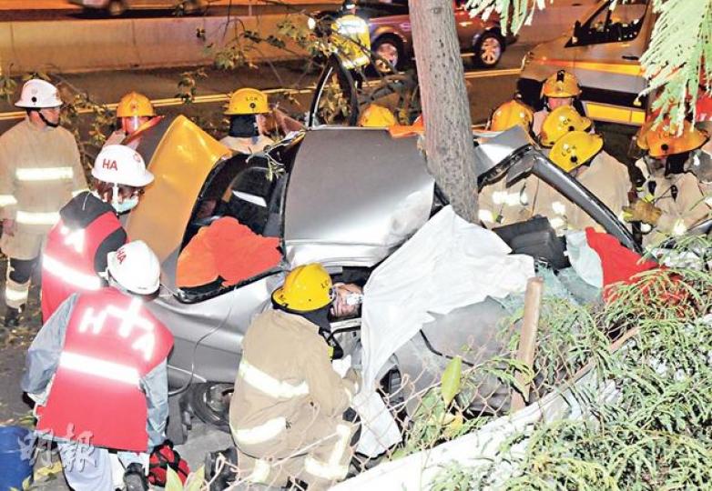 一輛改裝私家車昨凌晨高速駛至長沙灣警署對開時，失控直撞圖中大樹，私家車嚴重扭曲，司機被困車廂，由消防一邊安慰一邊救出。（蔡方山攝）