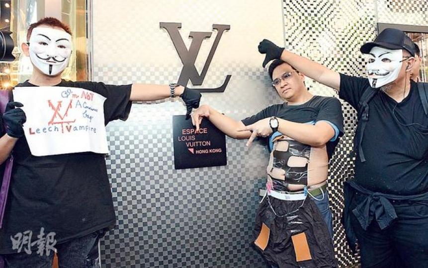 網民發起的「千人圍LV」行動，昨日活動開始時僅得3人現身，包括兩名戴上「V煞」面具的網民，及鄧簡文（中），身穿「格仔腹肌裝」以諷刺LV指使用格仔設計商戶侵權。（陳淑安攝）