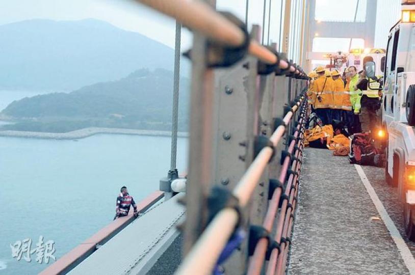 蓄「崩頭」髮型的30歲男子昨晨爬到青馬大橋邊緣危坐(左下),消防及警員不斷游說他返回安全位置,惟他1個多小時後突然躍下,幸獲救奇蹟不死。(蔡方山攝) 蓄「崩頭」髮型的30歲男子昨晨爬到青馬大橋邊緣危坐(左下),消防及警員不斷游說他返回安全位置,惟他1個多小時後突然躍下,幸獲救奇蹟不死。(蔡方山攝)
