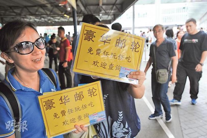 尖沙嘴天星碼頭外多名男女手持用簡體字寫着「豪華郵輪，免費任玩任吃」的宣傳牌，以招徠內地遊客。（尹錦恩攝）
