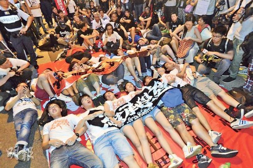 學民思潮昨由政府總部前往中聯辦，至金鐘道時一度被警方阻截，學民不滿，多人一度躺卧馬路抗議。（鄧宗弘攝）學民思潮抵達中聯辦後，由於中聯辦並無派員接信，成員要爬上鐵馬，以將印有標語的橫額（圖右橙色）及其遊行聲明拋進中聯辦內。（鄧宗弘攝）