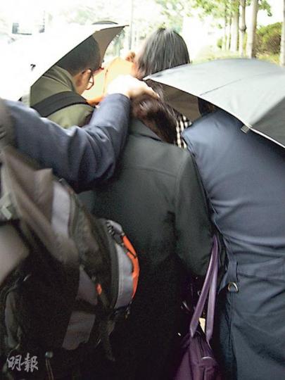 被控公職人員行為失當的被告袁慧妝(圖中被手按頭者),昨戴上口罩並由多名親友「分工合作」護送離開法庭,包括1人負責指揮、3人負責舉起「雨傘陣」遮擋鏡頭,其餘數人則負責開路及阻擋記者。(黃建邦攝) 被控公職人員行為失當的被告袁慧妝(圖中被手按頭者),昨戴上口罩並由多名親友「分工合作」護送離開法庭,包括1人負責指揮、3人負責舉起「雨傘陣」遮擋鏡頭,其餘數人則負責開路及阻擋記者。(黃建邦攝)