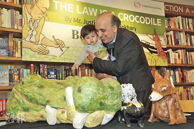 終審法院非常任法官包致金（右）手抱20月大男孫Zane（左）出席其新書《The Law is a Crocodile》的發布兼簽名會，其間他帶孫兒「滿場飛」，又讓孫兒欣賞由他親手用廢紙製作的書中主角公仔，包括鱷魚（左下起）、鼬鼠及狐狸，不過孫兒對「大場面」顯得有點害羞。（郭慶輝攝）