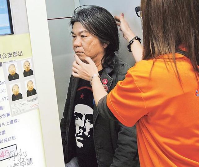 社民連立法會議員梁國雄「長毛」（左）昨往中旅社辦理「出入境通行證」，其間由現場職員「親自指導」正確影快相姿勢。（李紹昌攝）