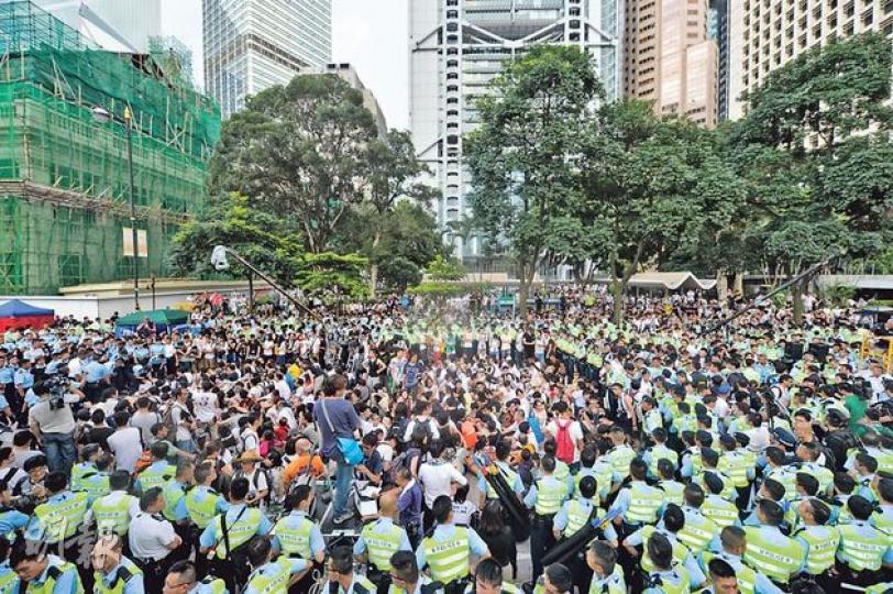 警方昨凌晨3時起在中環遮打道開始清場，至昨晨仍有100多人未被抬走（圖中央），大批警員不斷推前封鎖線，收窄封鎖範圍，現場亦有市民圍觀及聲援示威者，整個行動至8時半左右完成。警方拘捕511人，包括學生、教授、七旬長者，前高官廖秀冬的媳婦也在被捕之列。（鄧宗弘攝）警方昨接近凌晨3時清場，至天光後仍有百多名留守「預演佔中」的市民未被抬走，在場女警將到場示威的理大社會科學前副教授何芝君（中，白衫者）抬起，帶往附近的旅遊巴送往黃竹坑警校。（余俊亮攝）警方清場行動中，一般有4名警員抬走1名示威者，但昨現場所