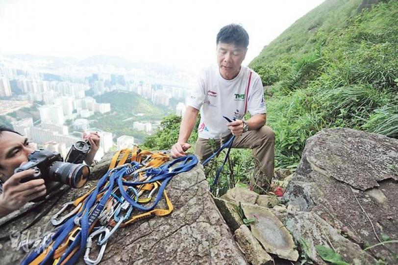 攀山專家鍾建民到場了解事件，檢獲死者遺下的攀石裝備，其中一條藍色扁帶有整齊切口（手持者），疑是勒過死者頸部，消防員救人時割斷。（余思朗攝）發生奪命意外的石壁，攀石發燒友稱之為「skyline crag」（天際岩），昨午意外後，仍有外籍夫婦到場攀石。（衛永康攝）
