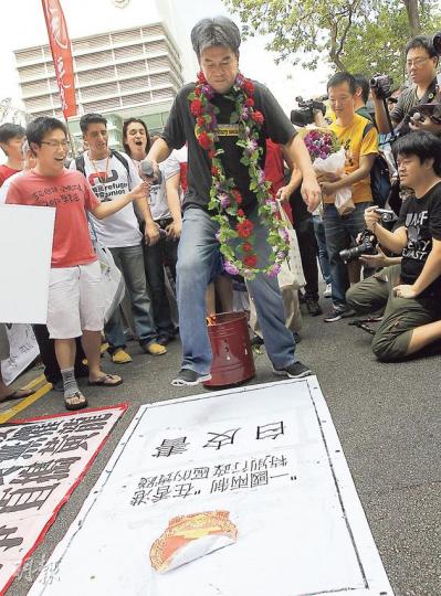 社民連成員昨日準備了多本「一國兩制在港實踐」白皮書，拋進火盆供剛出獄的梁國雄（中）跨過，再踐踏巨型「白皮書」以示抗議。有梁的支持者送上鮮花，甚至放花炮慶祝。（李紹昌攝）（明報製圖）