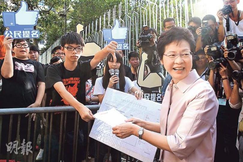 學民思潮成員昨日趁政務司長林鄭月娥(前右)到港台,以及政制及內地事務局長譚志源赴商台節目時,向二人派送「道具成績表」。剛領取DSE成績單的學民成員黃之鋒及周庭,給予林太的「成績」,數學(遊行統計學)是U;中國語文(閱讀中央旨意)考得5**,而語言偽術及體育(搬龍門)也是5**。林鄭月娥則回應,「恭喜你們文憑試考得不錯,希望你們繼續學業」。黃之鋒追問民間投票或民建聯民調是否具有認受性,林太指政改諮詢報告已如實歸納民意。她收下請願信,拒收道具成績單。而黃之鋒在旁倒豎拇指。(林俊源攝)佔中發起人戴耀廷 學民思潮成員昨日趁政務司長林鄭月娥(前右)到港台,以及政制及內地事務局長譚志源赴商台節目時,向二人派送「道具成績表」。剛領取DSE成績單的學民成員黃之鋒及周庭,給予林太的「成績」,數學(遊行統計學)是U;中國語文(閱讀中央旨意)考得5**,而語言偽術及體育(搬龍門)也是5**。林鄭月娥則回應,「恭喜你們文憑試考得不錯,希望你們繼續學業」。黃之鋒追問民間投票或民建聯民調是否具有認受性,林太指政改諮詢報告已如實歸納民意。她收下請願信,拒收道具成績單。而黃之鋒在旁倒豎拇指。(林俊源攝)佔中發起人戴耀廷