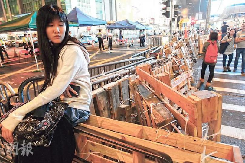 入夜後的彌敦道與亞皆老街交界的路障，左邊只有幾名警察在帳篷下站崗，右邊沒有防守佔領者，行人自由過馬路，氣氛輕鬆。一個少女若無其事把路障當櫈坐。（郭慶輝攝）