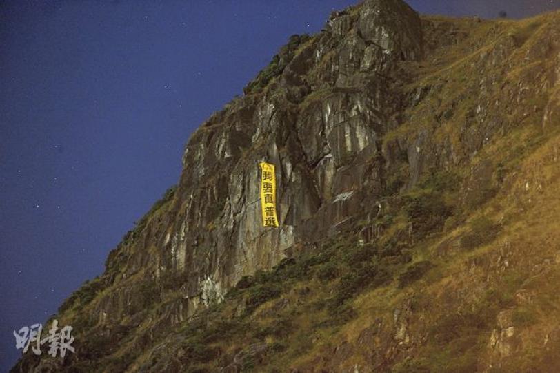 身分未明的攀山高手昨日在飛鵝山「自殺崖」掛上「我要真普選」巨型直幡，入黑後在清水灣道一帶仍清晰可見。（樊銳昌攝）