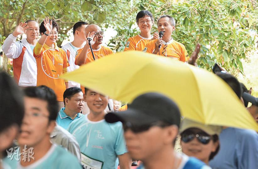 政務司長林鄭月娥(後左二)昨日身穿橙黃色上衣,出席新世界百貨苗圃挑戰12小時2014起步禮,有參加者在她面前撐起佔領運動象徵物黃色雨傘,林太繼續向人群揮手微笑。(盧翊銘攝) 政務司長林鄭月娥(後左二)昨日身穿橙黃色上衣,出席新世界百貨苗圃挑戰12小時2014起步禮,有參加者在她面前撐起佔領運動象徵物黃色雨傘,林太繼續向人群揮手微笑。(盧翊銘攝)