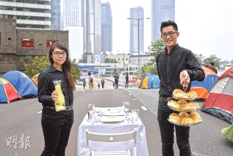 兩名香港教育學院學生昨在金鐘佔領區舉行一場藝術創作宴會,頭盤由菠蘿包開始,到最後一道菜為「真菠蘿」一片,寓意由假普選方案開始,冀爭取到真普選。圖為創作學生鄭同學(右)與阿Ca(左),阿Ca手持其中一道「溫水煮娃娃菜」。(余俊亮攝) 兩名香港教育學院學生昨在金鐘佔領區舉行一場藝術創作宴會,頭盤由菠蘿包開始,到最後一道菜為「真菠蘿」一片,寓意由假普選方案開始,冀爭取到真普選。圖為創作學生鄭同學(右)與阿Ca(左),阿Ca手持其中一道「溫水煮娃娃菜」。(余俊亮攝)