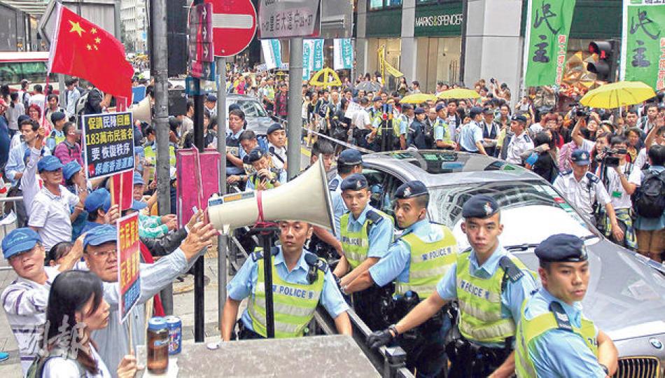 保衛香港運動約30名成員(左)於中環畢打街集會,跟民陣打對台,「藍」、「黃」陣營壁壘分明,警方築人鏈分隔雙方,中間留有一行車線讓車輛通過。(李澤彤攝)民陣昨發起遊行要求撤回人大決定,遊行人士抵達中聯辦後,分批於門外綁上黃絲帶。昨日亦有不少市民帶同象徵「雨傘運動」的黃傘遊行,社民連主席梁國雄(黑衣者)更把一把黃傘拋入中聯辦,門外警員舉手也阻止不及。(李澤彤攝) 保衛香港運動約30名成員(左)於中環畢打街集會,跟民陣打對台,「藍」、「黃」陣營壁壘分明,警方築人鏈分隔雙方,中間留有一行車線讓車輛通過。(李澤彤攝)民陣昨發起遊行要求撤回人大決定,遊行人士抵達中聯辦後,分批於門外綁上黃絲帶。昨日亦有不少市民帶同象徵「雨傘運動」的黃傘遊行,社民連主席梁國雄(黑衣者)更把一把黃傘拋入中聯辦,門外警員舉手也阻止不及。(李澤彤攝)