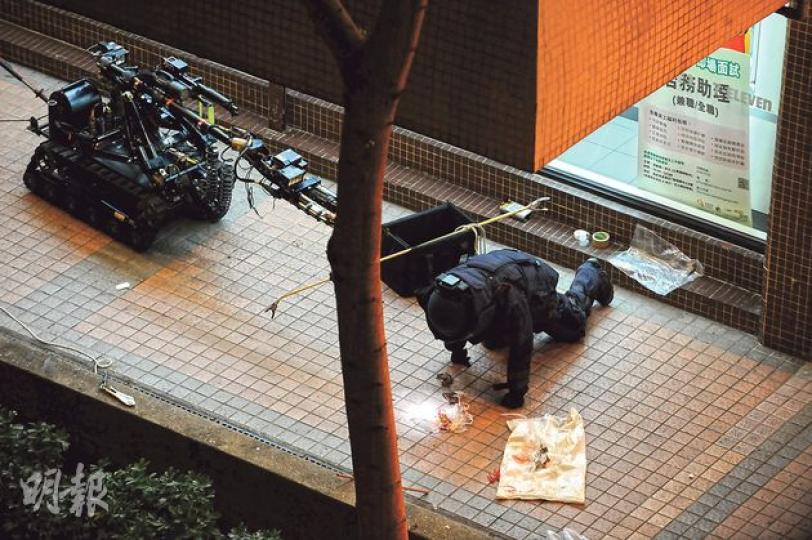 警方爆炸品處理課人員穿上全套保護衣到場，又派出一大一小的遙控拆彈機械人「獨眼龍」檢查涉事的紅色環保袋，消息指內有膠袋載着疑似燒鴨，內裏的不明物品曾發生爆炸。（樊銳昌攝）