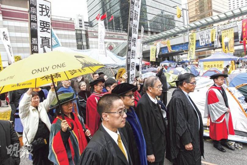 近百名大專學界教師及行政人員昨發起穿上學術袍或黑衣默站及遊行,有參與的教師舉起黃傘,其間經過金鐘佔領區時,引來佔領者和義工拍掌支持。(李紹昌攝) 近百名大專學界教師及行政人員昨發起穿上學術袍或黑衣默站及遊行,有參與的教師舉起黃傘,其間經過金鐘佔領區時,引來佔領者和義工拍掌支持。(李紹昌攝)
