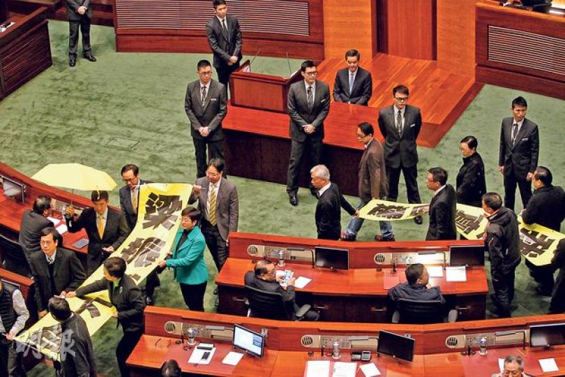 特首梁振英(講台後)昨日到立法會宣讀任內第三份《施政報告》,他甫進場泛民已刻意背對他,又不斷被人民力量陳偉業及陳志全等謾罵、大聲叫口號;梁振英未開口讀施政報告,再遇民主派議員舉起黃傘、拉起寫有「梁振英下台」、「我要真普選」字眼的黃色直幡抗議離場,令會議兩度中斷,擾攘10分鐘。一直笑對抗議的梁振英在復會後即「反擊」,稱「感謝全體反對派」給予他全程安靜的、應有的莊嚴環境宣讀施政報告。(郭慶輝攝) 特首梁振英(講台後)昨日到立法會宣讀任內第三份《施政報告》,他甫進場泛民已刻意背對他,又不斷被人民力量陳偉業及陳志全等謾罵、大聲叫口號;梁振英未開口讀施政報告,再遇民主派議員舉起黃傘、拉起寫有「梁振英下台」、「我要真普選」字眼的黃色直幡抗議離場,令會議兩度中斷,擾攘10分鐘。一直笑對抗議的梁振英在復會後即「反擊」,稱「感謝全體反對派」給予他全程安靜的、應有的莊嚴環境宣讀施政報告。(郭慶輝攝)