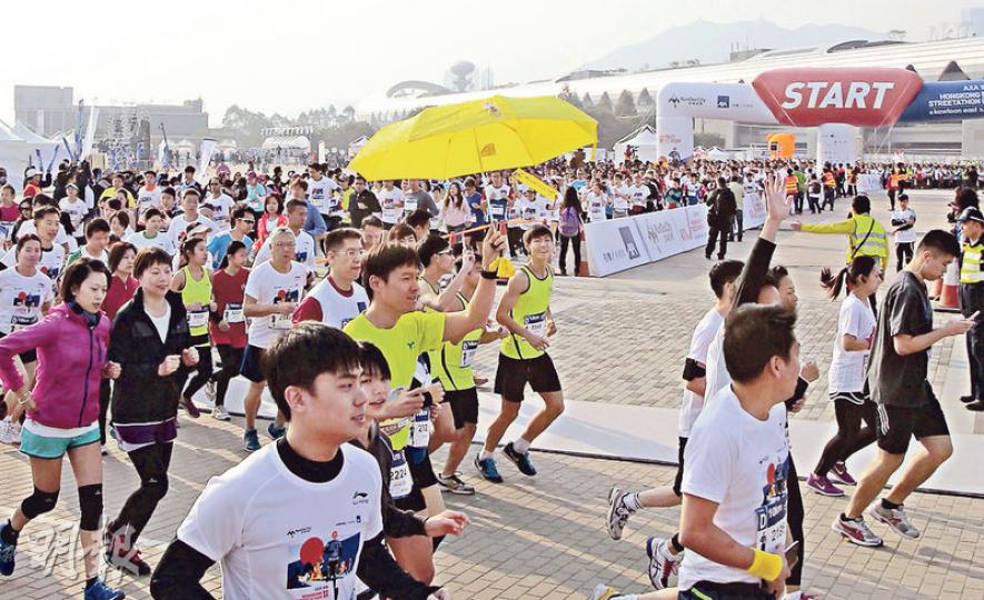 第二屆「香港街頭馬拉松」昨於啟德郵輪碼頭起步，途經觀塘海濱長廊及九龍灣住宅區，吸引超過8000名跑手參加，賽事包括10公里及新增的半馬拉松。有跑手身穿黃衣、撐黃傘參賽；有市民手持雨傘標語，向跑手派發「我要真普選」貼紙。（李澤彤攝）（明報製圖）