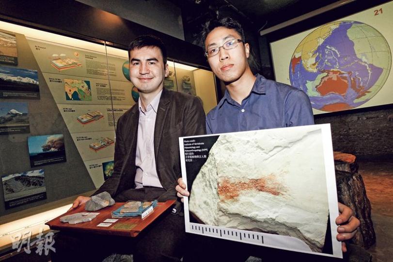 港大地球科學系一級榮譽畢業生謝子旗（右）在該系古脊椎研究所主管文嘉棋博士（左）等指導下，成功鑑別一塊在荔枝莊發現、屬侏羅紀時期「副狼鰭魚」化石（圖中手持相片）。（李紹昌攝）
