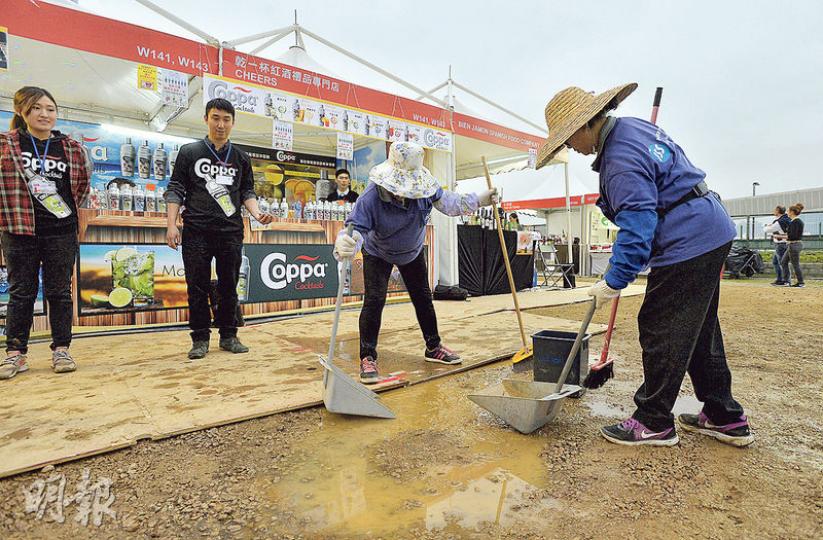 香港紅酒協會等多個團體首次舉辦「添馬紅酒佳餚節」暨「數碼生活嘉年華」昨起一連5天在中環添馬公園海濱舉行。因天雨影響，場地變成一片爛泥地，滿佈積水，多個攤位都要臨時鋪設木板，清潔工人亦忙於清理積水。不少參展商批評主辦單位準備支援不足，大半天也未能提供木板鋪地。（余俊亮攝）商戶心聲 - 食品商户鍾小姐：是次主辦單位非常不專業，由中午12時致電主辦方要求鋪木板，直到下午4時多都未有木板運到。租用場地的時候未有想過會一地泥濘。（余俊亮攝）