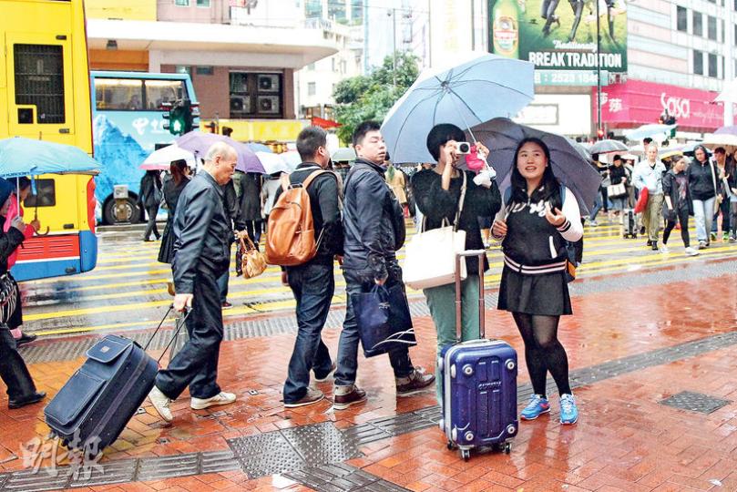 商界及旅遊界均認為，「一周一行」新措施對旅遊業及實體經濟無大影響，因為真正來港旅遊及間中購買日用品的內地客，本來就不會過於頻密訪港。圖為旅客昨冒雨在銅鑼灣街頭「拖筴」遊覽，拍照留念。（林俊源攝）