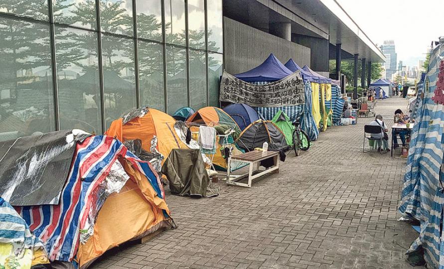 政總及立法會門外仍有約125個行山營及57個大帳篷,近日天氣炎熱,部分留守者將桌椅搬到帳篷外乘涼及交談。(張煒明攝) 政總及立法會門外仍有約125個行山營及57個大帳篷,近日天氣炎熱,部分留守者將桌椅搬到帳篷外乘涼及交談。(張煒明攝)