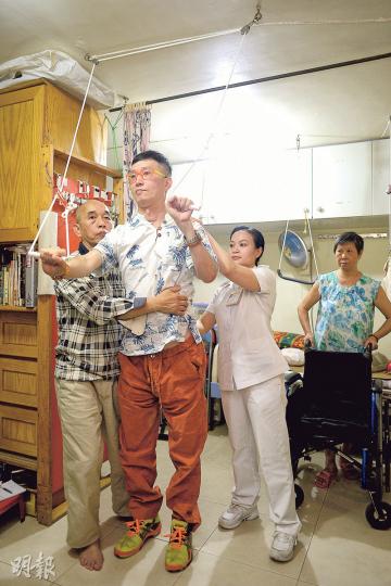 蔡爸（左一）運用自小砌模型的技巧「當模型咁砌」，將300多方呎的大埔公屋單位化成家居物理治療室，包括圖中家珏（左二）示範使用的「手拉繩」，儀器的滑輪及尼龍繩都是買的，手把則是蔡爸用廢棄的電線管改造。連身旁的物理治療師陸鳳妍（右二）也說佩服。蔡爸自豪地說，「那時醫生說（家珏）站的機會也沒有，現在可以放手（讓他站立）」，起碼可維持一兩秒。眾人身後的為蔡媽（右一），她說從沒把兒子當成傷殘，只當他是小孩。（余俊亮攝）
