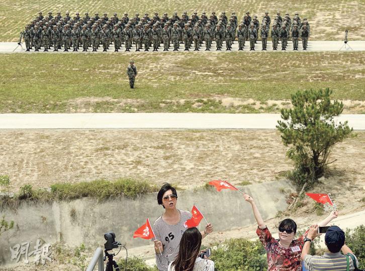 昨有逾500人獲邀觀看解放軍駐港部隊軍演，包括逾百名市民，未知屬何團體，他們觀看演練期間不時鼓掌，並興奮揮舞大會派發的區旗及國旗拍照。圖為歷時約45分鐘的軍演結束後，駐軍於中央平地列隊，有觀眾興奮揮動國旗與軍人「合照」。（余俊亮攝）