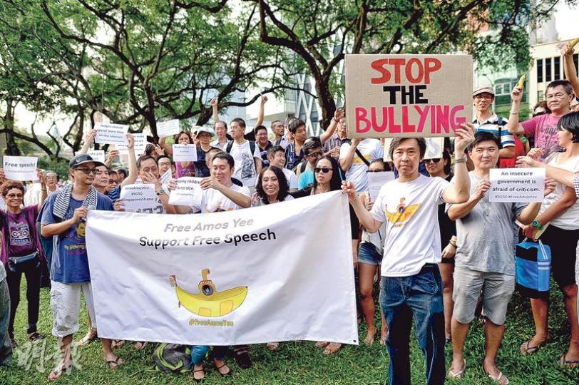 數以百計示威者昨午在新加坡芳林公園集會，要求釋放余澎杉，有市民舉起寫着「停止欺凌」的標語，主辦者聲稱有500人參加昨日集會。（明報記者攝）新加坡社運人士韓慧慧昨在芳林公園集會現場撐起黃傘，她說曾受邀在不同地方出席講座，今年6月曾到香港，得悉黃傘象徵民主及自由，遂帶同出席昨日集會，傘上更有「平反六四」等字句。（明報記者攝）