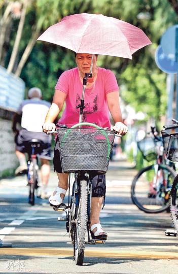 在酷熱天氣警告下，有市民在大埔騎單車也做足防曬措施，打傘乘風而行，以免中暑。（蘇智鑫攝）