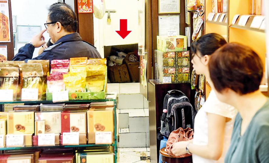 現場所見，竊匪把分店木製後門下方鋸開（箭嘴示）潛入犯案，得手後原路爬行逃走，避過紅外線感應。（蔡方山攝）警員到場調查，在大廈天井位置視察竊匪潛入店舖的路線。（蔡方山攝）警方調查後，相信匪徒是沿天井外牆水渠爬落位元堂分店後門位置。（蔡方山攝）現場所見，位元堂分店被竊匪搜掠後一片凌亂，被偷藥材全部擺放在櫃枱較低位置，部分藥材散落地上。（蔡方山攝）